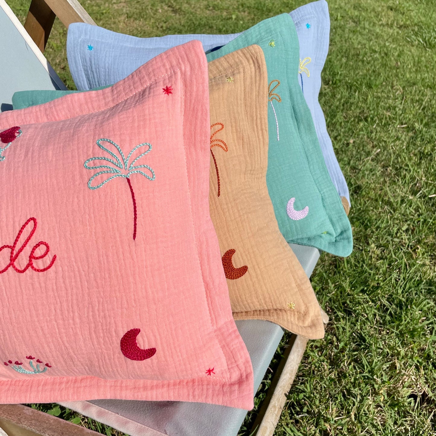 Coussins de naissance personnalisés brodés à la main dans des coloris doux inspirés de la Savane, présentés en extérieur au soleil de Provence.