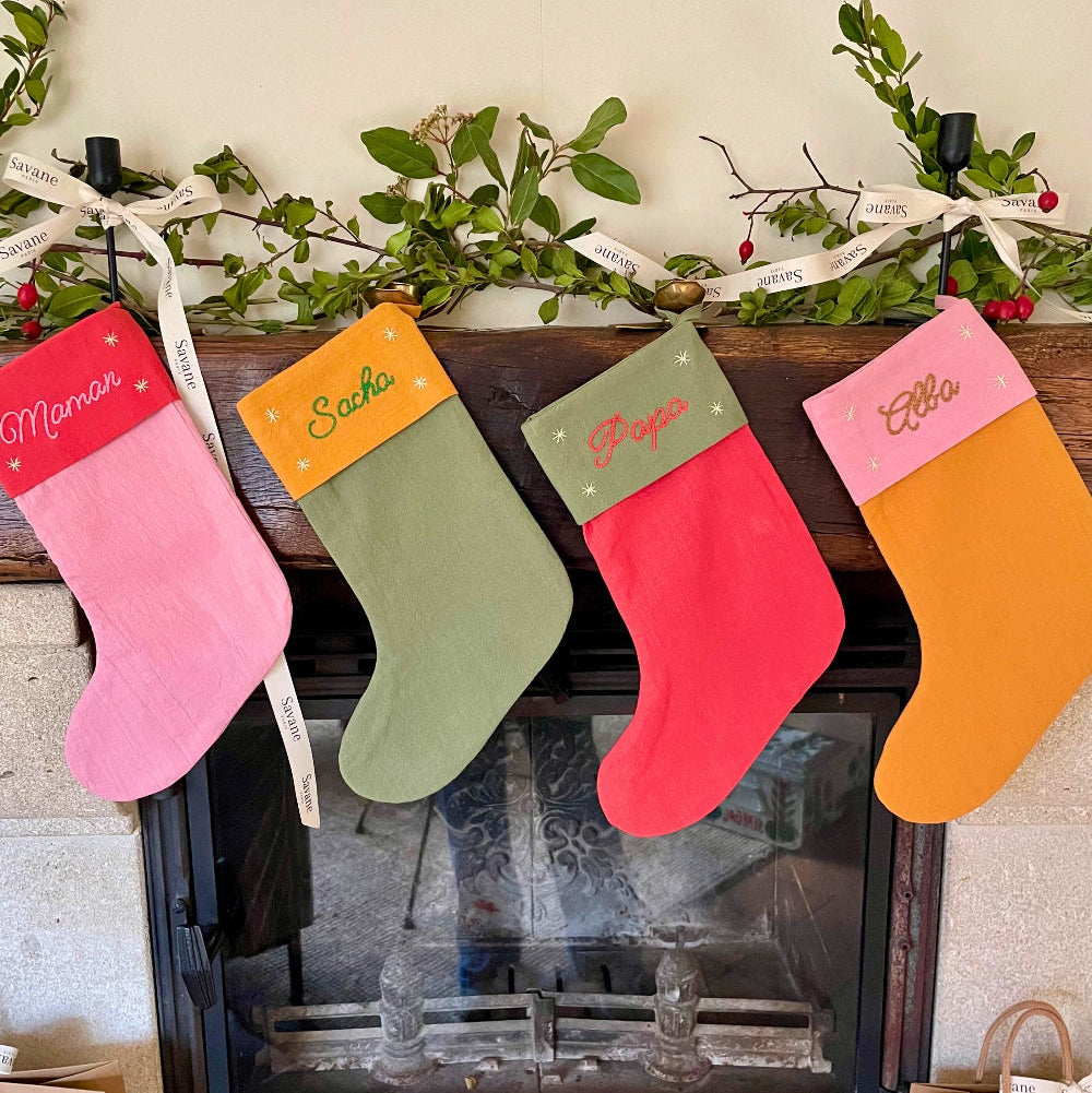 Ensemble de chaussettes de Noël personnalisées brodées main : Maman, Sacha, Papa et Alba. Créations artisanales Savane Paris en coton lavé, coloris assortis, suspendues sur une cheminée – édition limitée fabriquée en France.