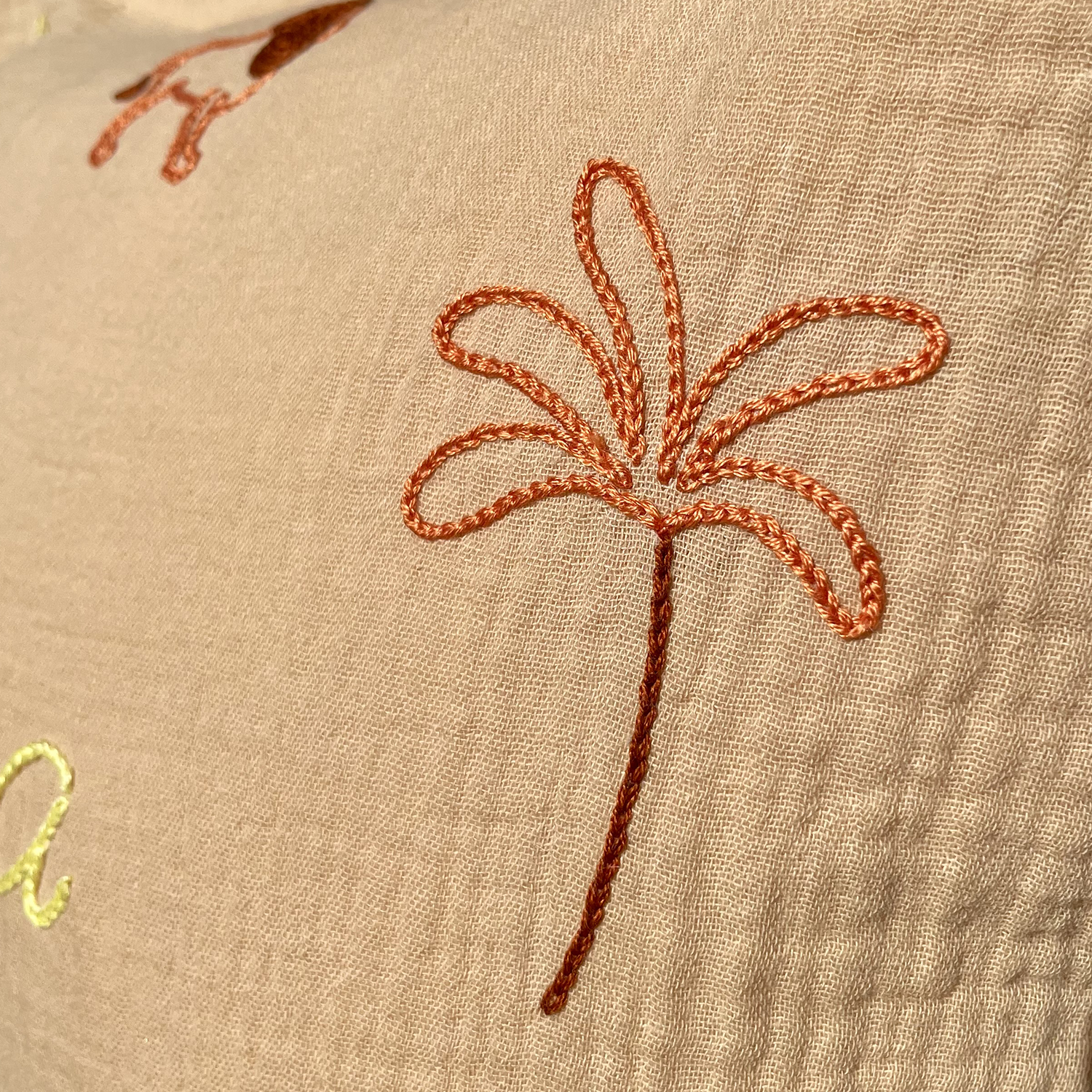Détail de la broderie palmier réalisée à la main sur un coussin de naissance beige en gaze de coton Savane Paris
