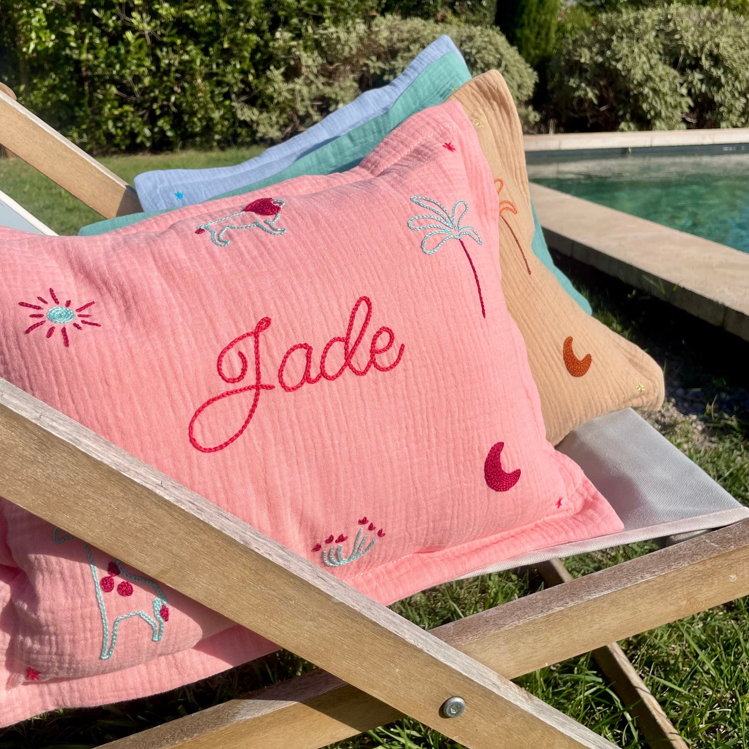 Coussin de naissance personnalisé Jade en gaze de coton rose, brodé à la main avec prénom, lion, palmier, lune et motifs savane au point de chaînette.