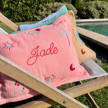 Coussin de naissance personnalisé Jade en gaze de coton rose, brodé à la main avec prénom, lion, palmier, lune et motifs savane au point de chaînette.