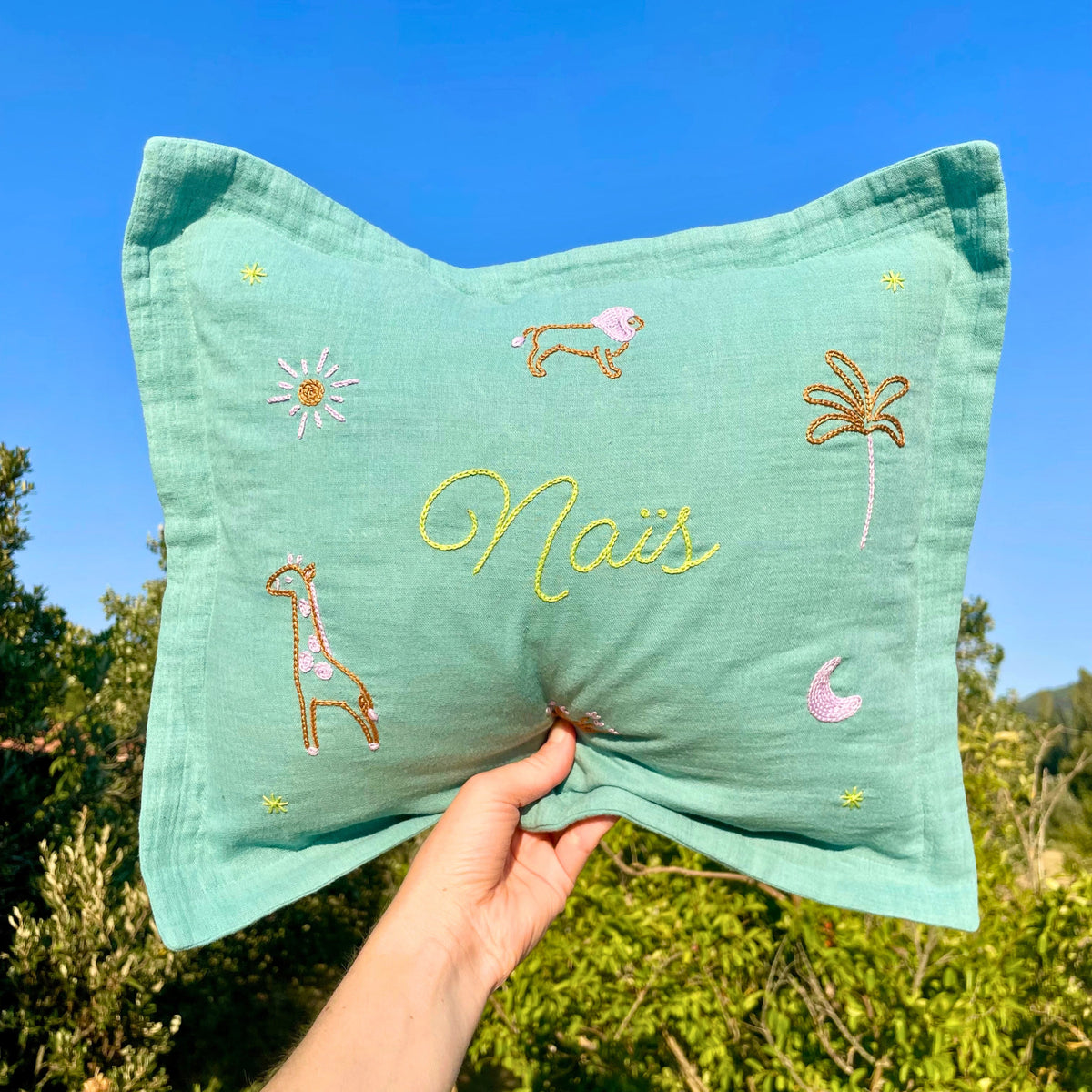 Coussin bébé personnalisé vert doux au prénom Naïs, brodé à la main avec girafe, lion, palmier et lune rose.