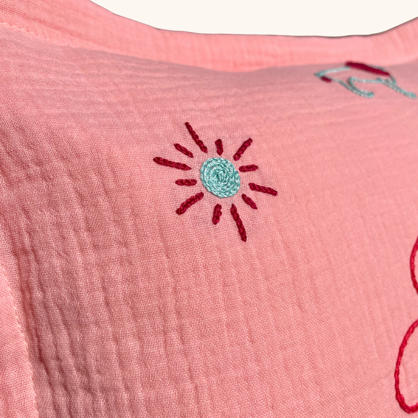 Détail de la broderie soleil sur coussin de naissance rose Savane Paris, broderie faite main en France sur gaze de coton.
