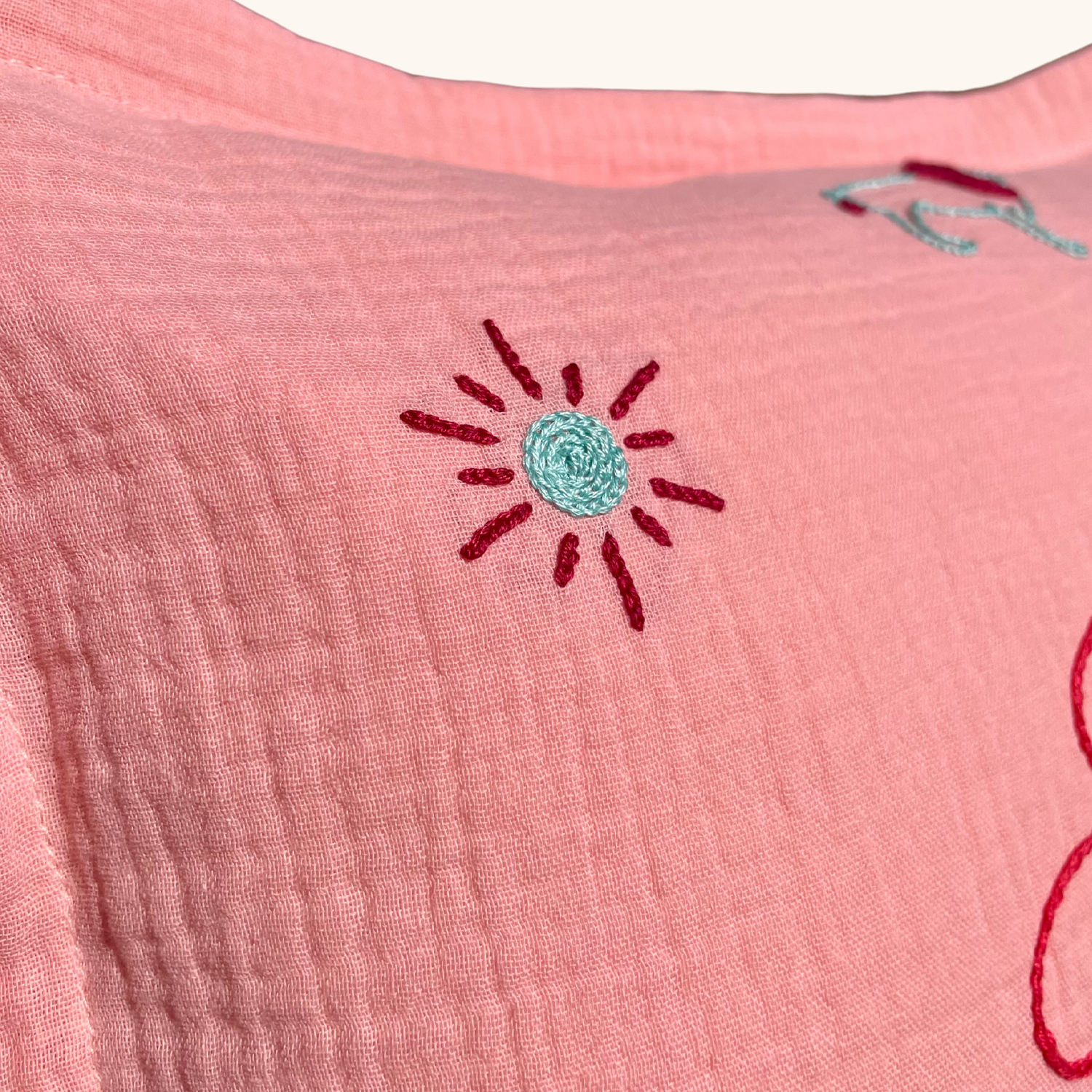 Détail de la broderie soleil sur coussin de naissance rose Savane Paris, broderie faite main en France sur gaze de coton.