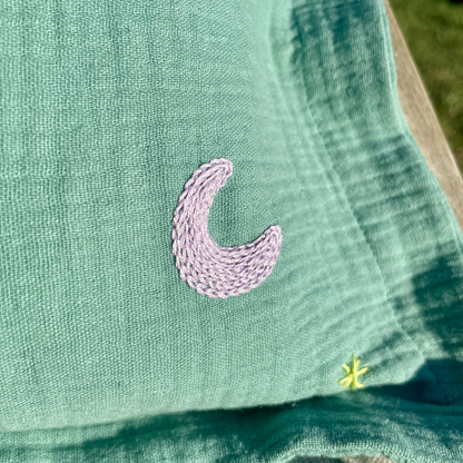 Détail de la broderie lune réalisée à la main sur un coussin de naissance vert en gaze de coton Savane Paris
