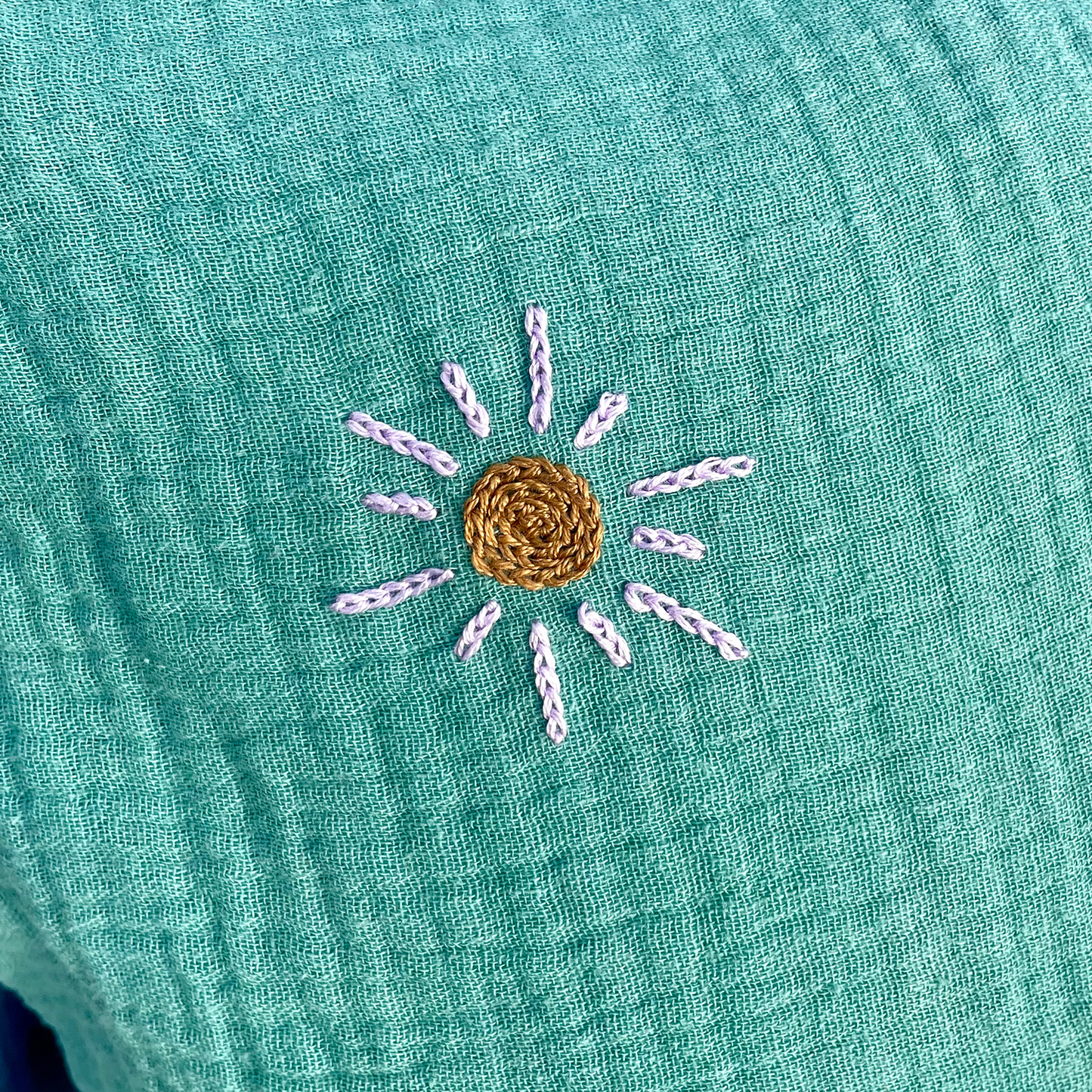 Broderie soleil artisanale au point de chaînette sur coussin de naissance vert en gaze de coton Savane Paris
