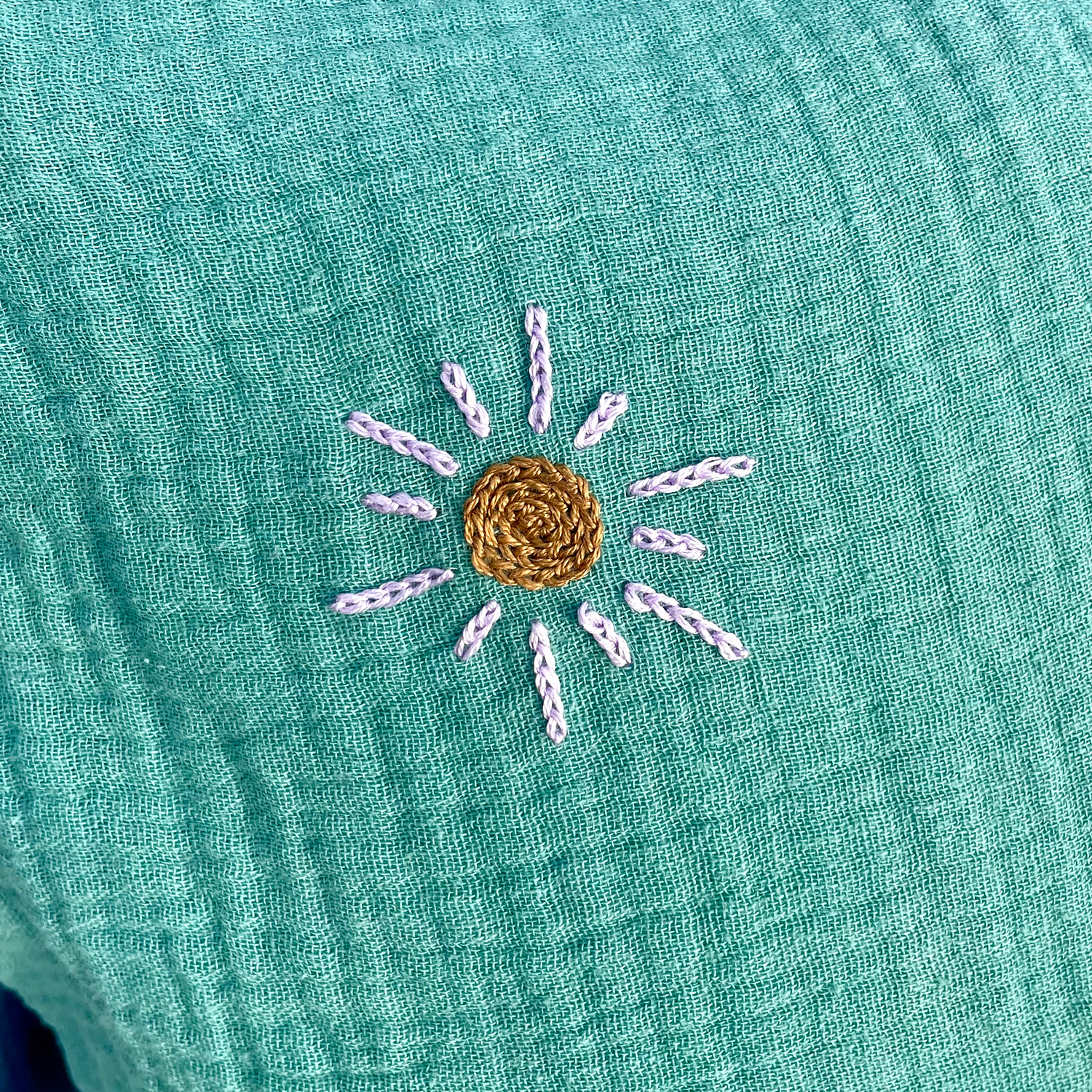 Broderie soleil artisanale au point de chaînette sur coussin de naissance vert en gaze de coton Savane Paris
