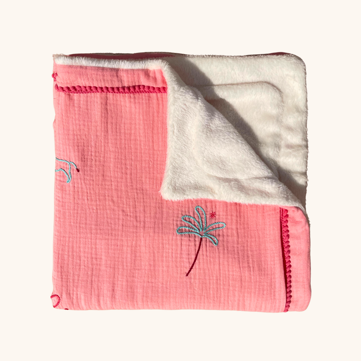 Détail d'une couverture de naissance en double gaze de coton rose, avec doublure blanche moelleuse et palmier brodé.