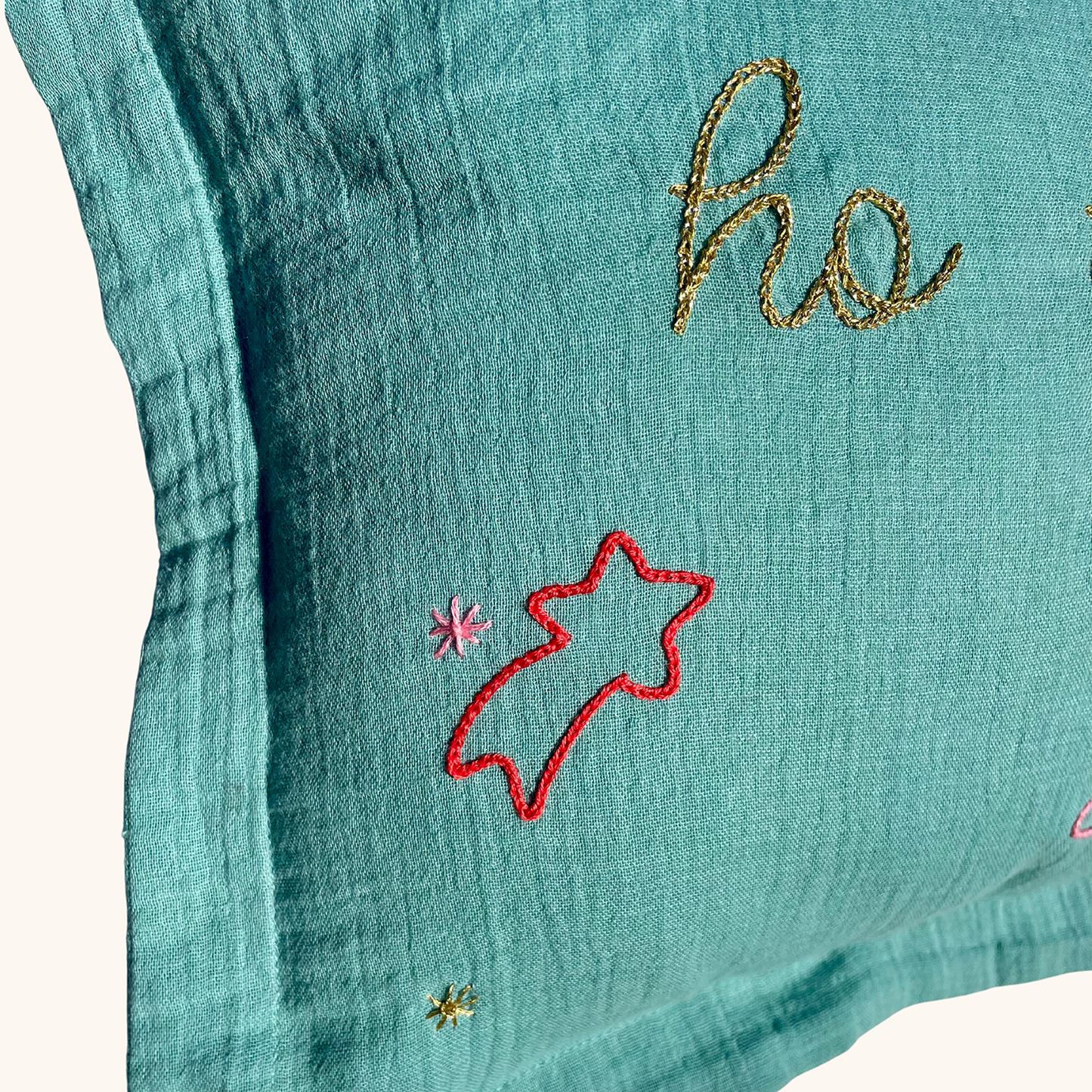 Zoom sur la broderie étoile filante et fil doré “ho” d’un coussin de Noël vert fait main en France, édition limitée Savane Paris.
