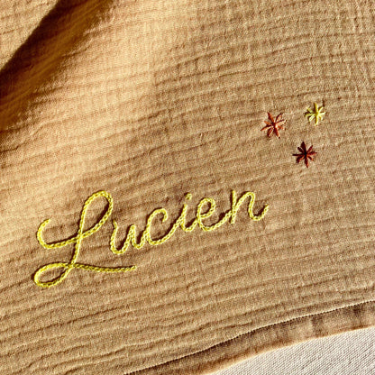 Détail de la broderie au point de chaînette sur un lange beige en gaze de coton, réalisée à la main dans l’atelier Savane Paris.