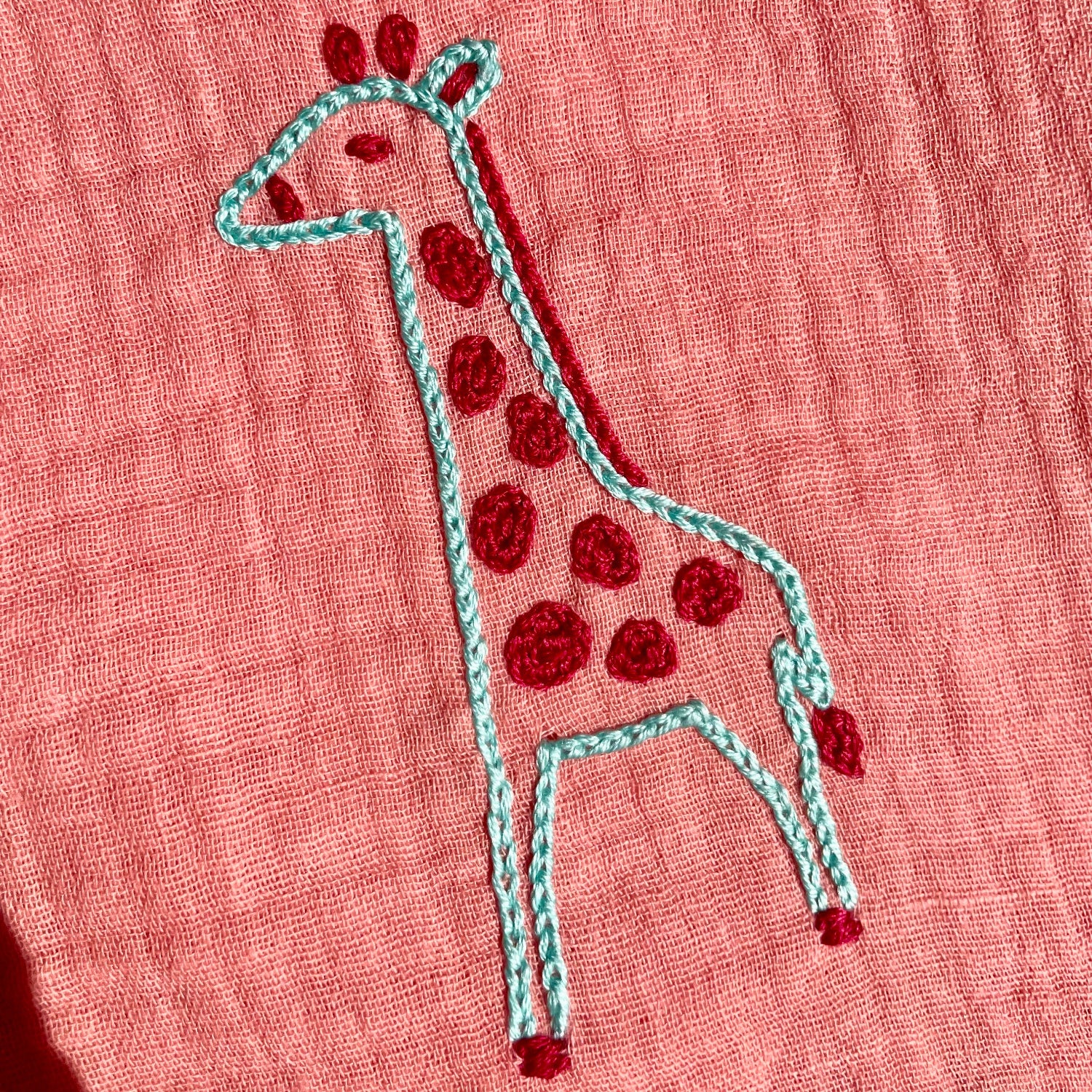 Détail de la girafe brodée à la main au point de chaînette sur un lange personnalisé Savane, création artisanale pour bébé.