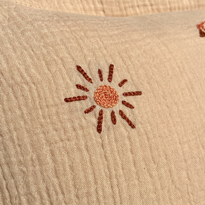 Gros plan sur la broderie soleil et fil DMC sur coussin de naissance beige en gaze de coton, création artisanale Savane Paris.