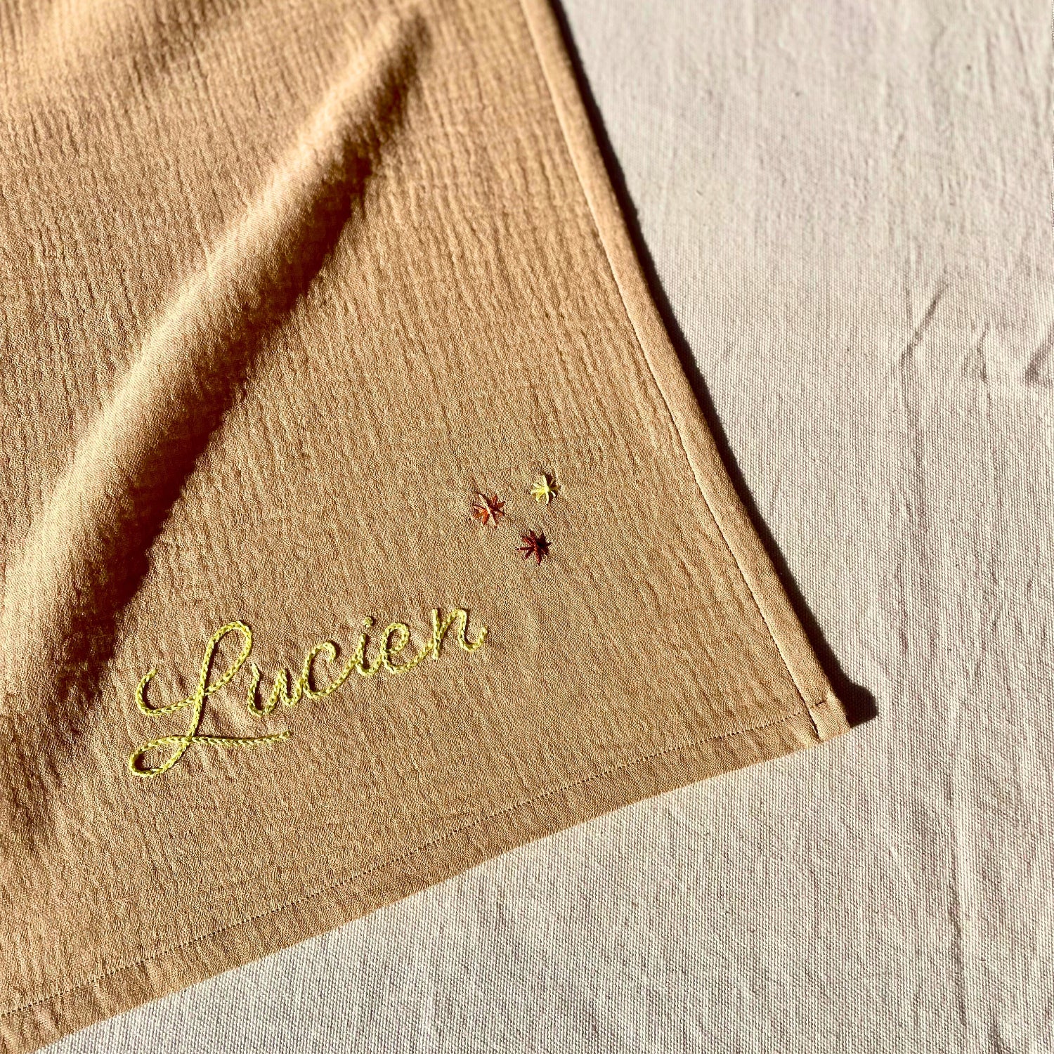 Zoom sur la broderie du prénom et des étoiles sur un lange beige personnalisé, brodé à la main en France par Savane Paris.