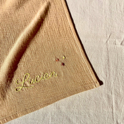 Zoom sur la broderie du prénom et des étoiles sur un lange beige personnalisé, brodé à la main en France par Savane Paris.
