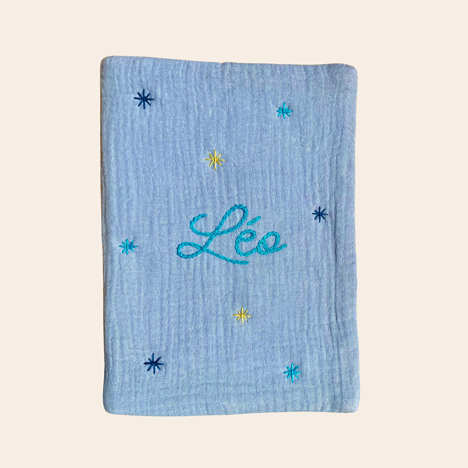 Protège carnet de santé bébé personnalisé bleu ciel, brodé à la main au prénom et orné de petites étoiles – création artisanale Savane Paris, fabriquée en France en gaze de coton.