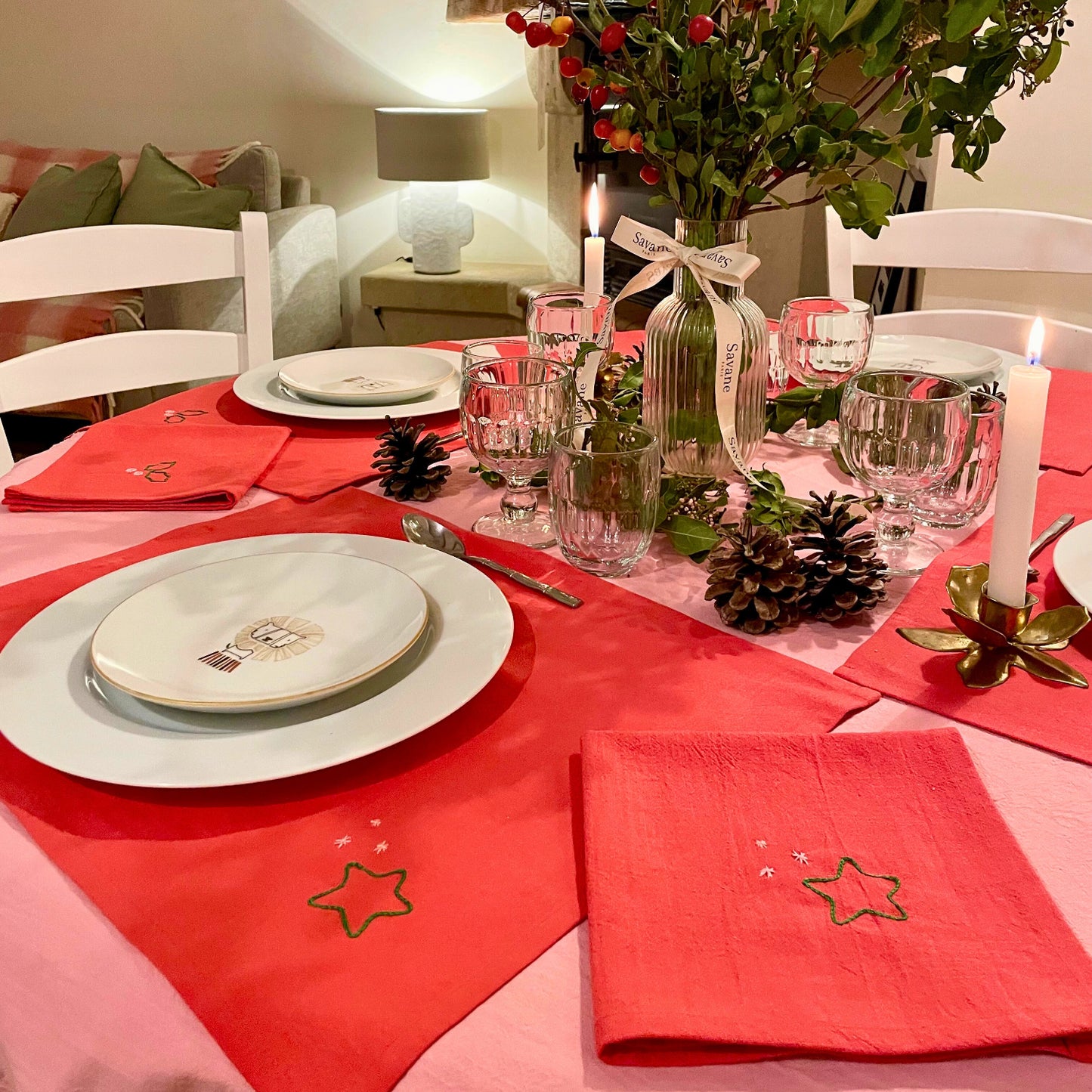 Table de Noël Savane Paris dressée avec sets et serviettes rouges brodés, ambiance chaleureuse dans la maison de Noël, décoration artisanale made in France.