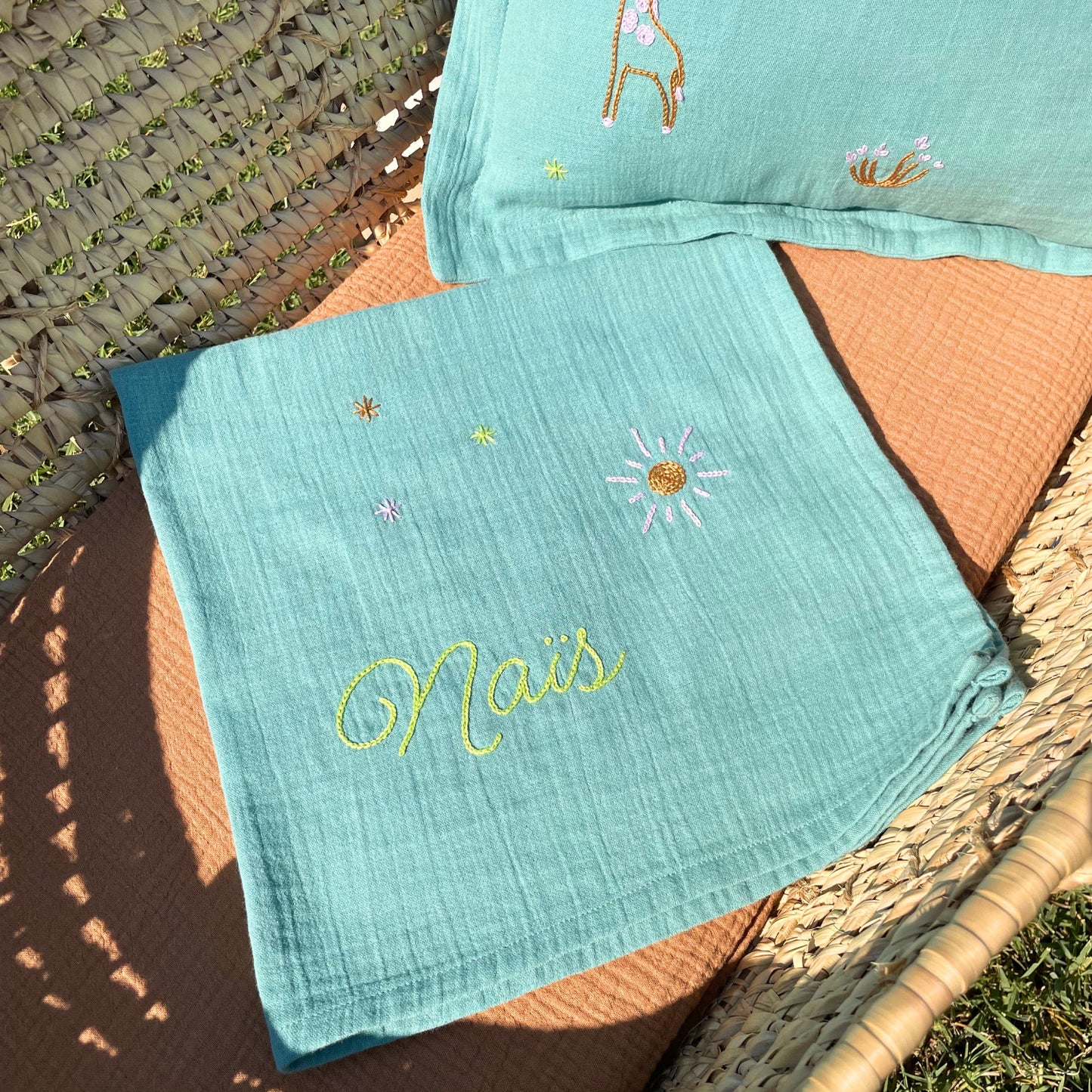 Trousseau de naissance Savane composé d'un lange personnalisé et d'un coussin brodés à la main au point de chaînette dans un atelier à Marseille.