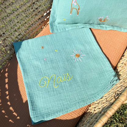 Trousseau de naissance Savane composé d'un lange personnalisé et d'un coussin brodés à la main au point de chaînette dans un atelier à Marseille.