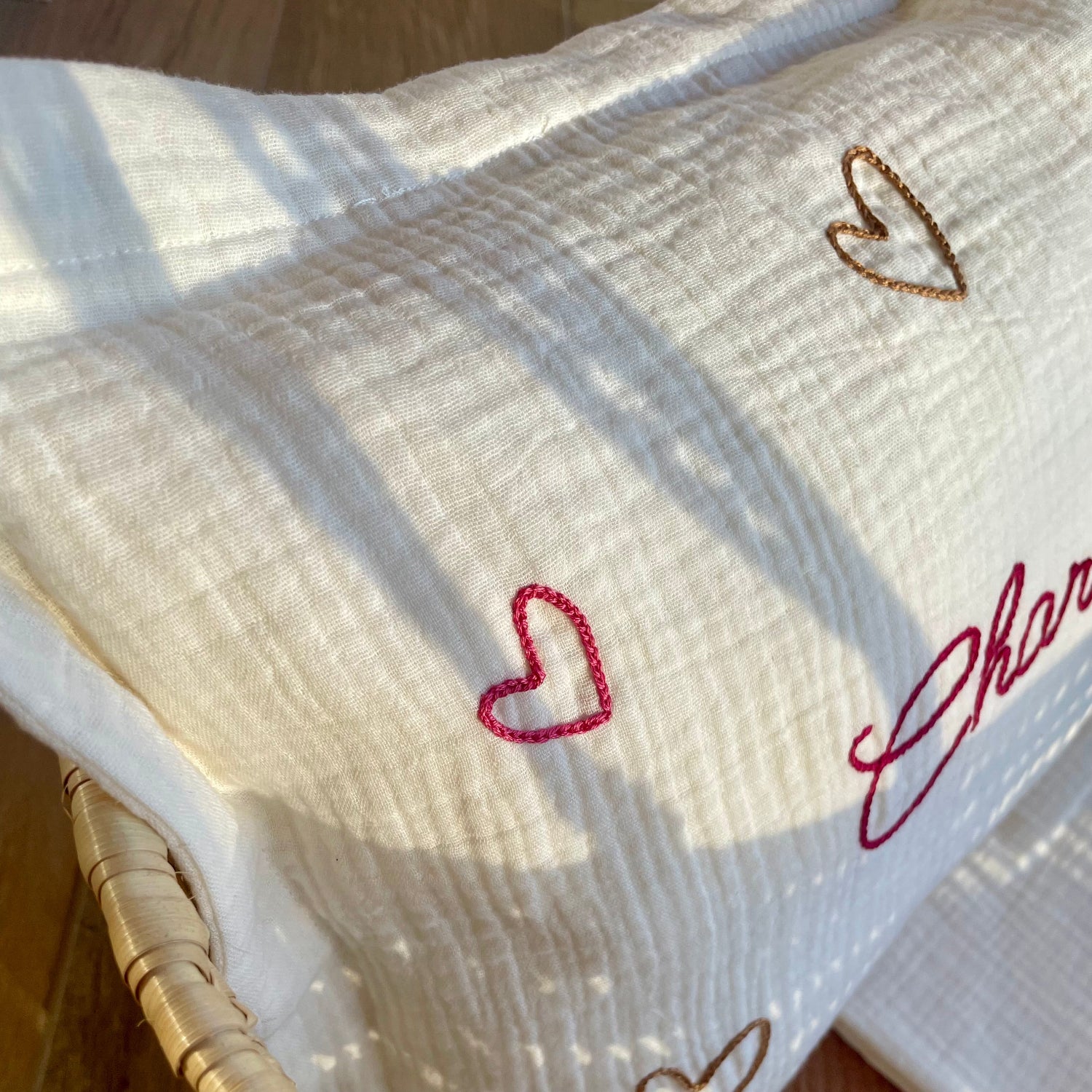 Zoom sur la broderie de petits cœurs cousue à la main sur un coussin de naissance personnalisé, collection Petits Cœurs Savane, broderie artisanale au point de chaînette.