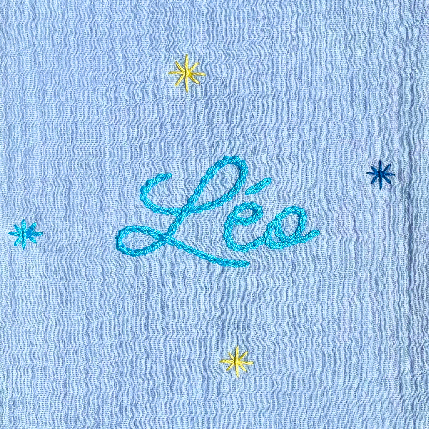 Zoom sur la broderie du prénom réalisée à la main sur un protège carnet de santé bleu cielSavane Paris – fil DMC, savoir-faire artisanal français, cadeau de naissance personnalisé.