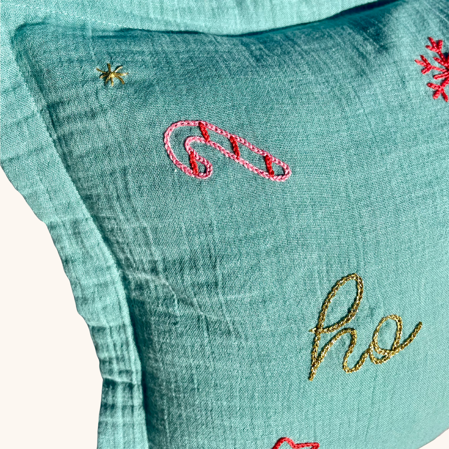 Gros plan sur la broderie sucre d’orge et fil doré sur coussin de Noël vert en gaze de coton, création artisanale et édition limitée Savane Paris.