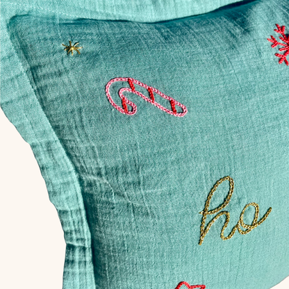Gros plan sur la broderie sucre d’orge et fil doré sur coussin de Noël vert en gaze de coton, création artisanale et édition limitée Savane Paris.